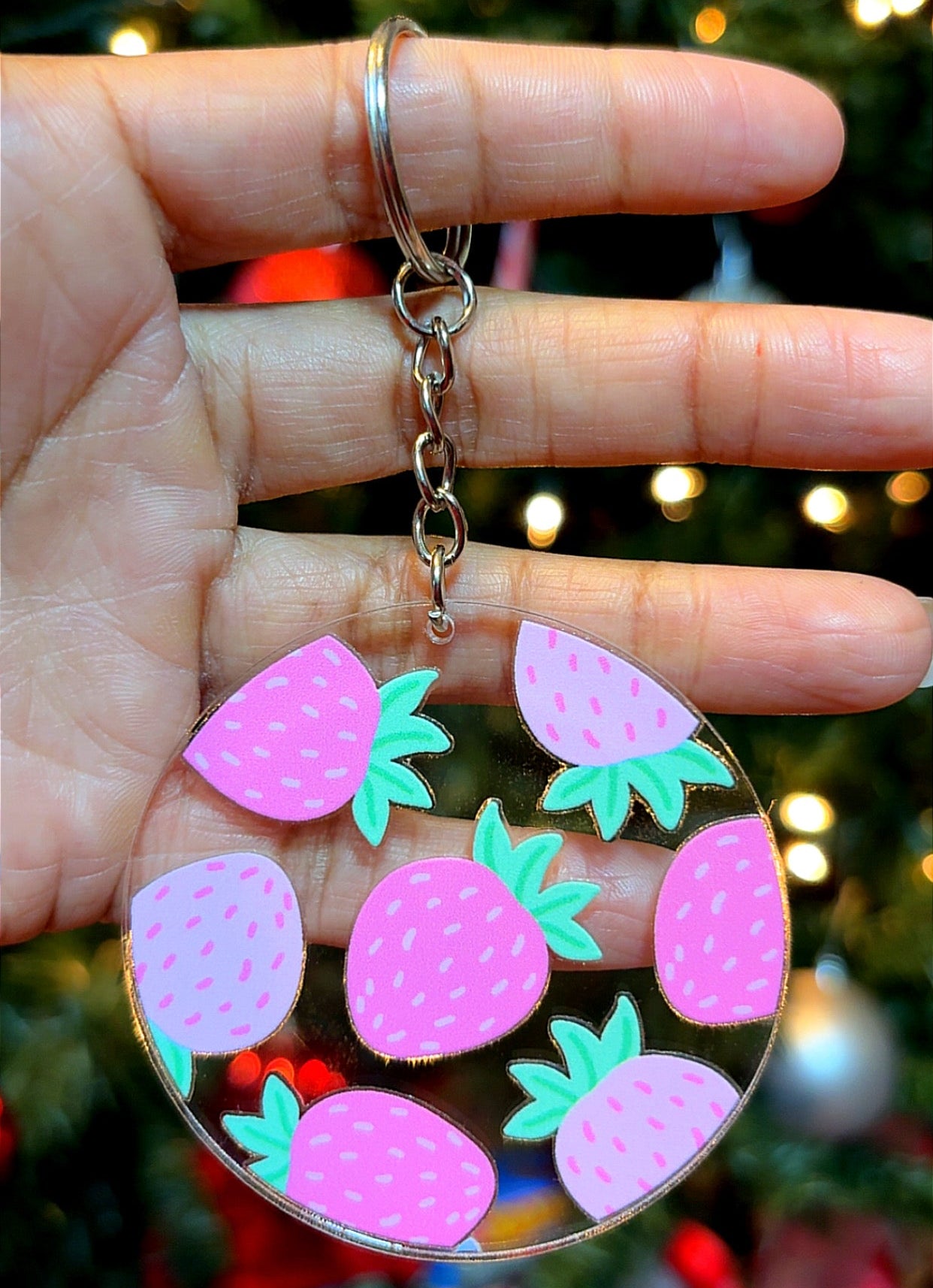 Keychain with pink strawberry design held in front of a Christmas tree.