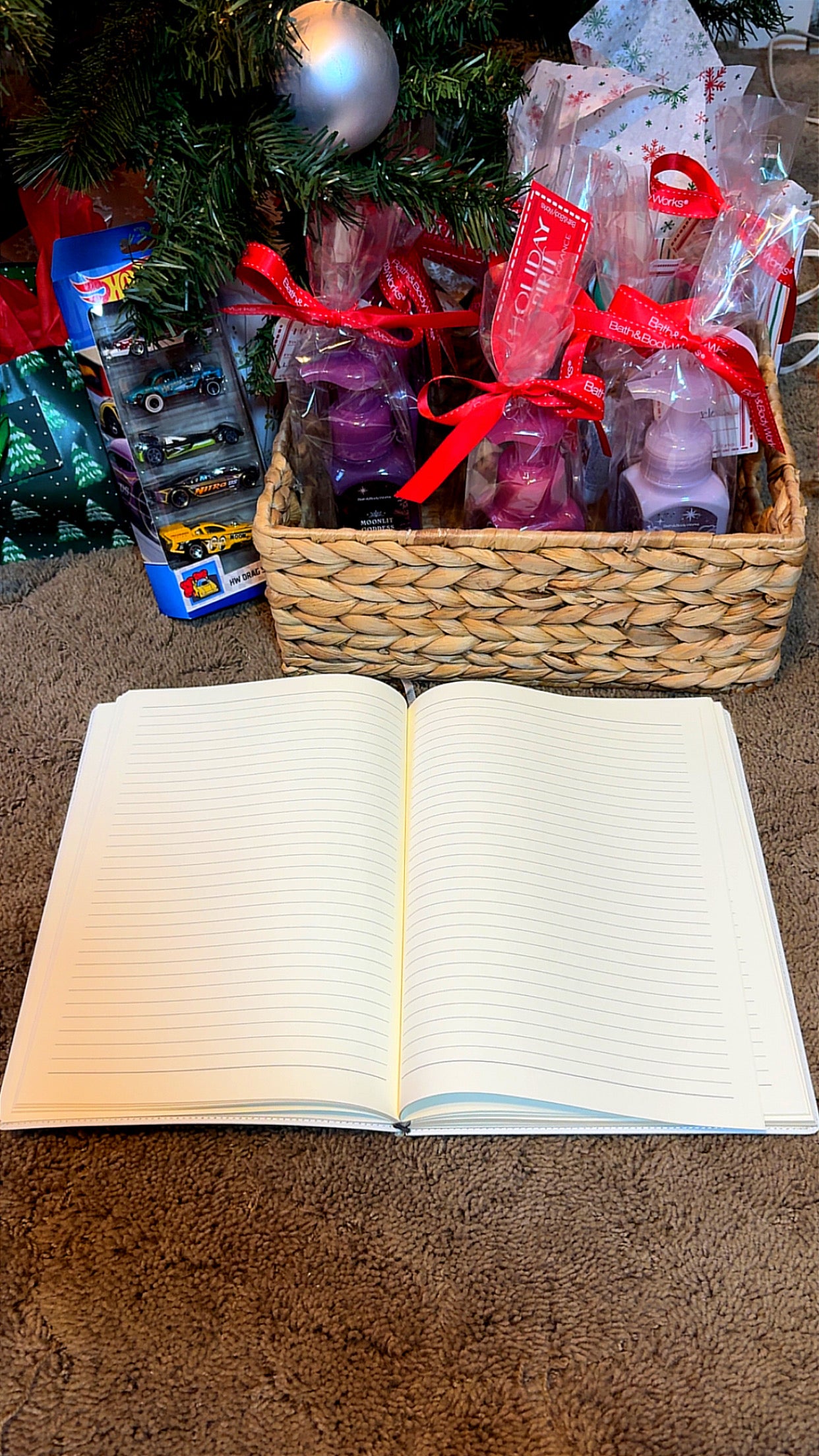 Open notebook next to a gift basket under a decorated Christmas tree.
