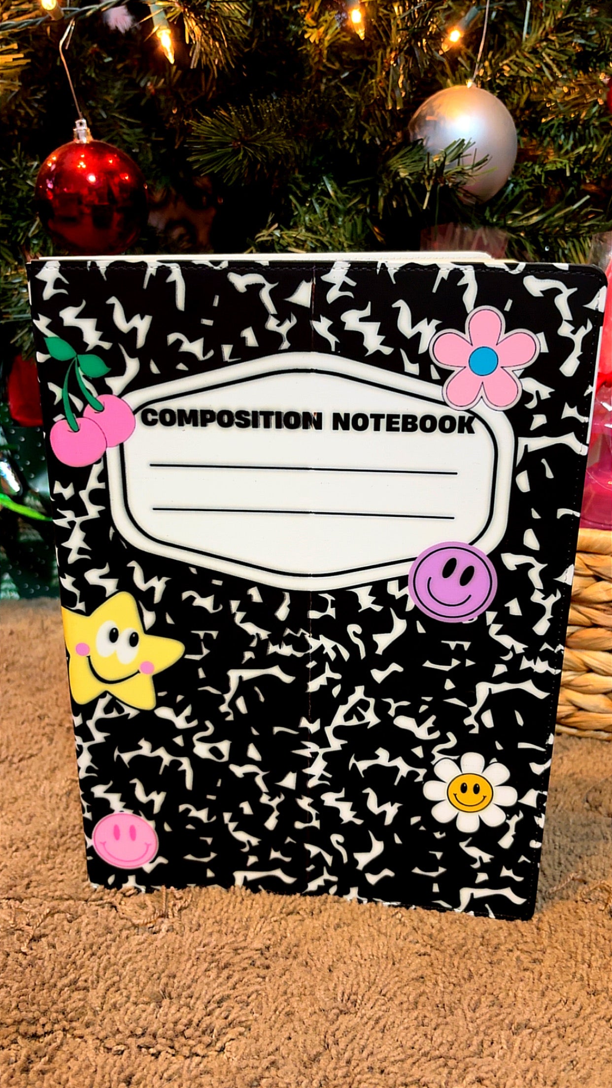Composition notebook with decorative stickers against a Christmas tree background