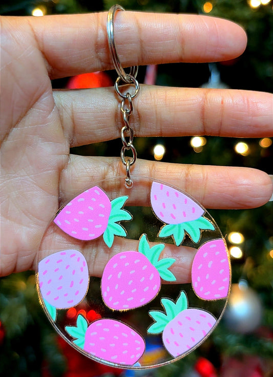 Keychain with pink strawberry design held in front of a Christmas tree.