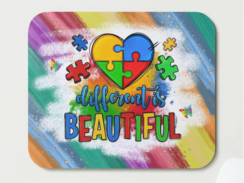 Colorful mouse pad with a heart-shaped puzzle piece design and 'different is beautiful' text on a rainbow background.