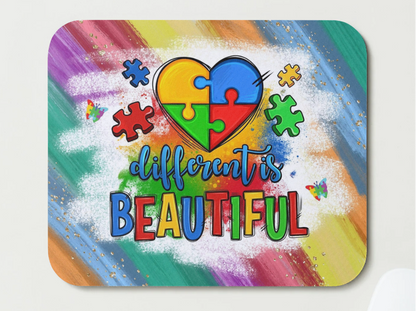 Colorful mouse pad with a heart-shaped puzzle piece design and 'different is beautiful' text on a rainbow background.
